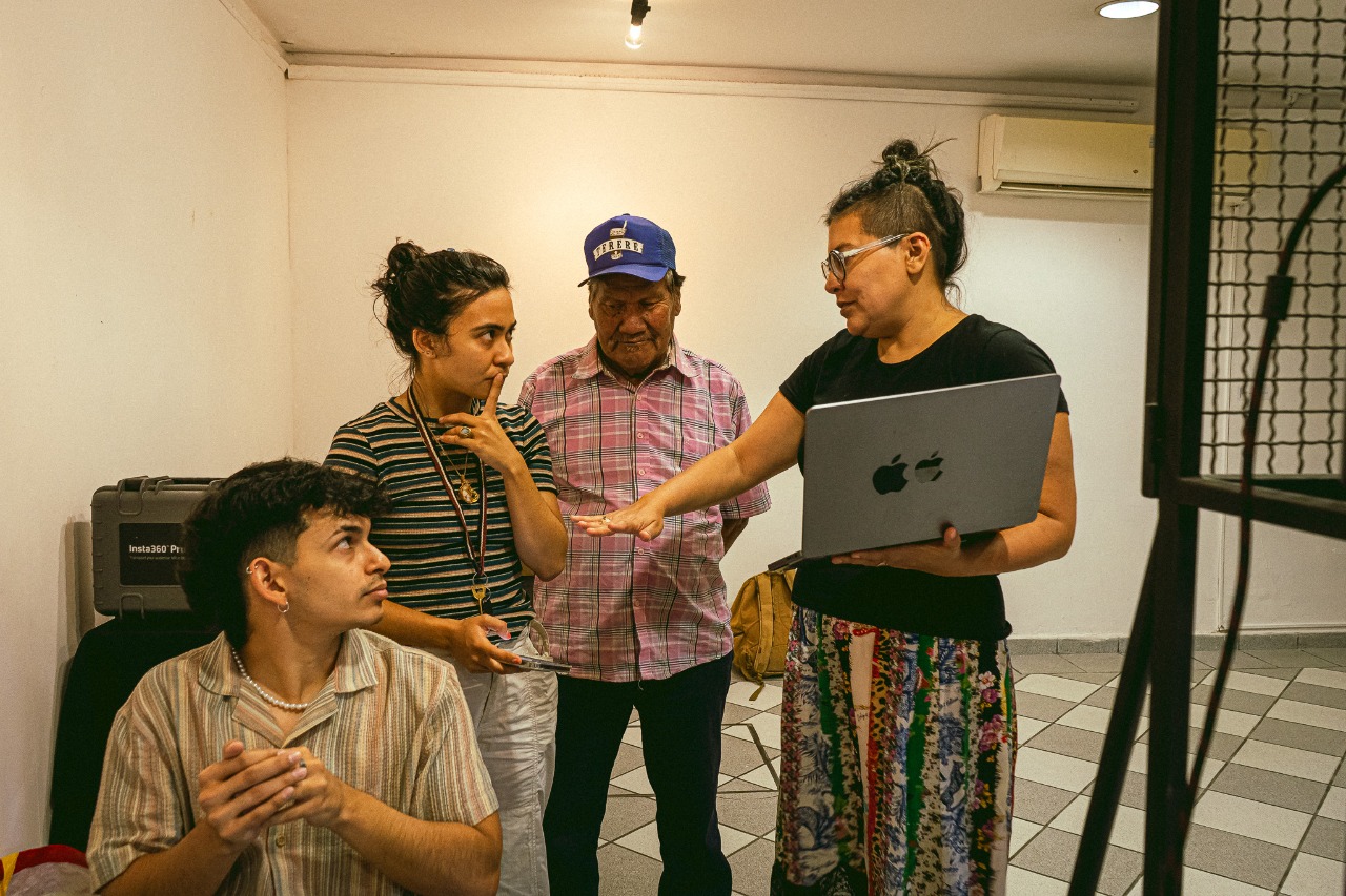 Equipo y participantes de EXPYLAB 2022 conversando alrededor de una MacBook durante una sesión de revisión de material, con caja Insta360 Pro a la vista, en la Mediateca de la Alianza Francesa