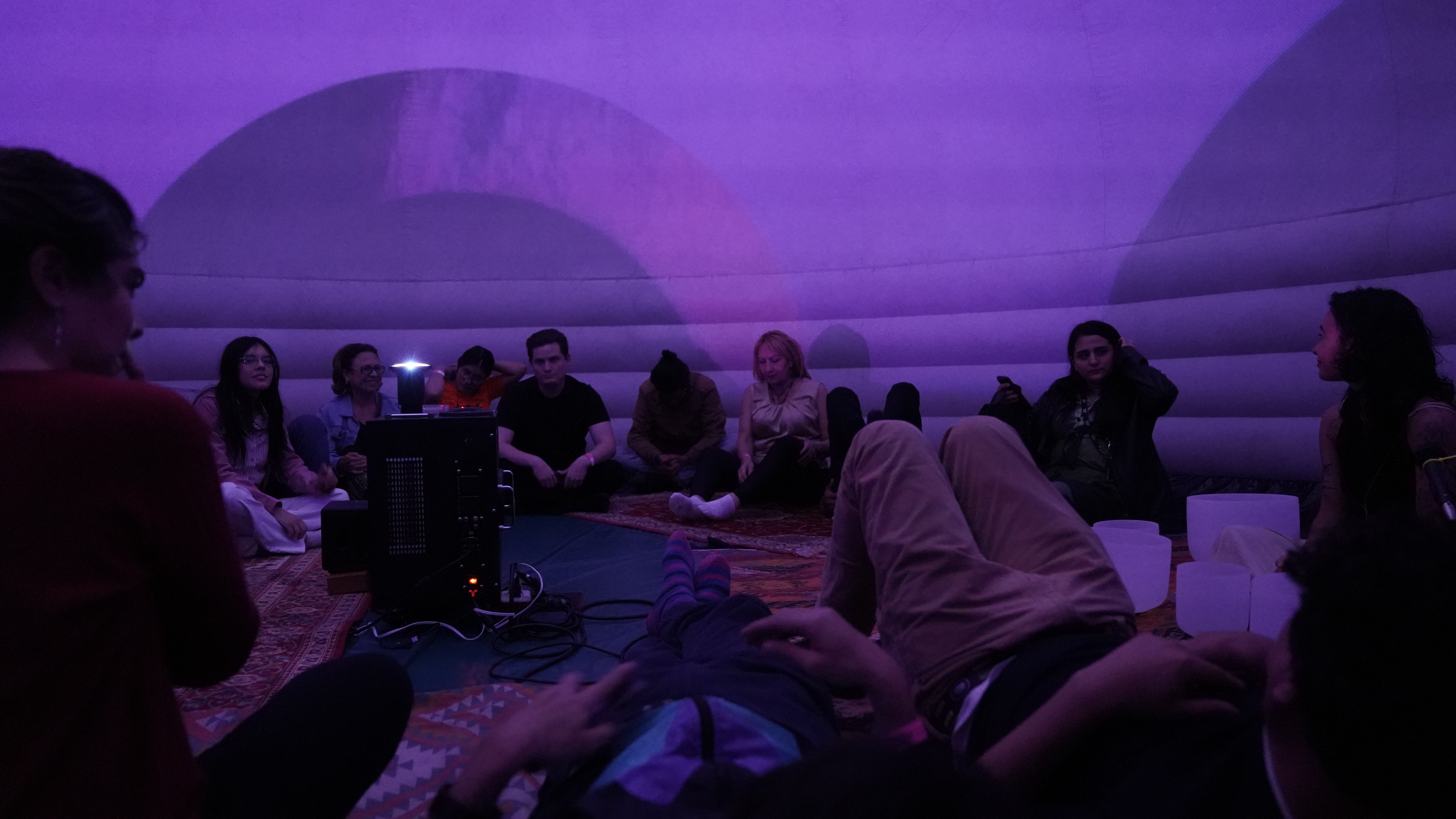 Experiencia inmersiva en cúpula inflable púrpura del EXPYLAB — participantes sentados sobre alfombras alrededor de un proyector central, con cuencos sonoros y proyecciones suaves
